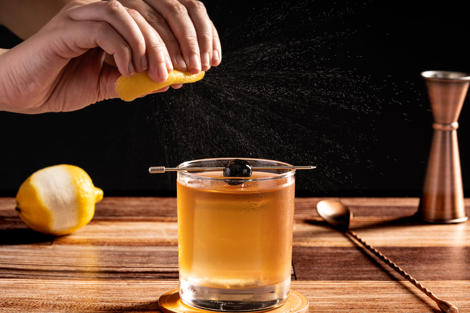 A bartender zesting a lemon over the Quiet Professional cocktail, an Old Fashioned variation made with Four Branches Bourbon, amaretto, and maple syrup.