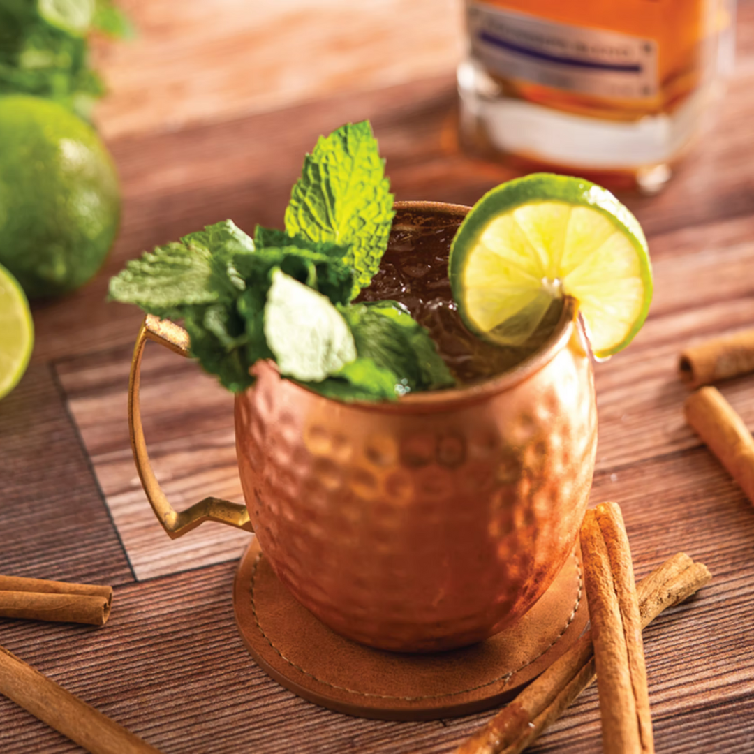 Randy Couture’s Toll Road cocktail served in a copper mule glass, garnished with mint sprig and lime wheel beside Four Branches Bourbon.