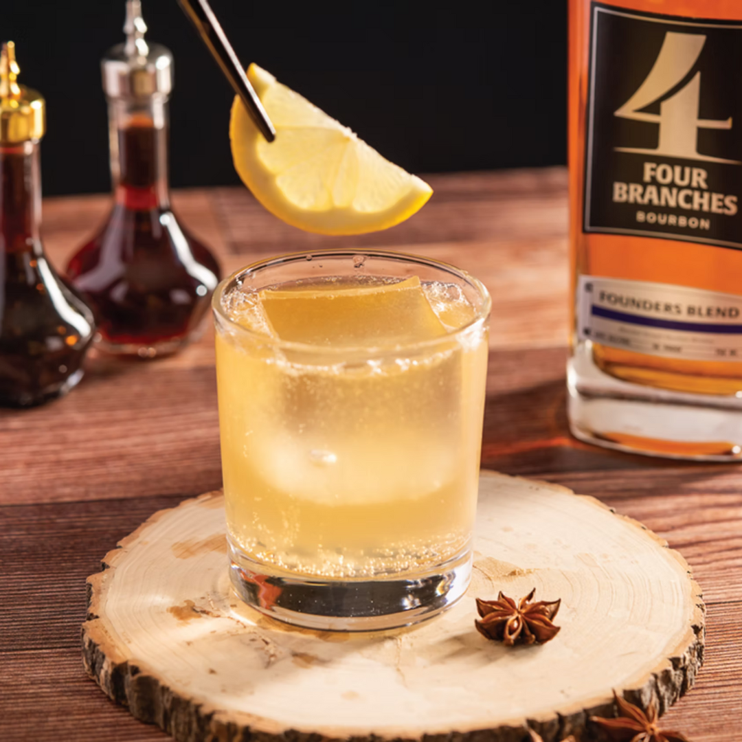 The Tempest bourbon cocktail topped with ginger ale, garnished with a lemon slice, served in a rocks glass beside Four Branches Bourbon.