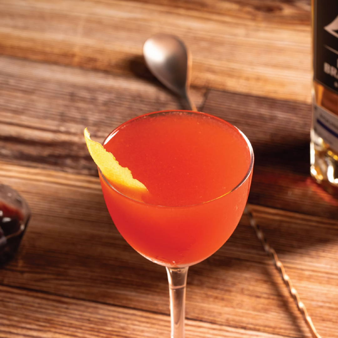 Top Gun bourbon cocktail with Aperol, Amaro, and lemon served in coupe glass with lemon twist garnish